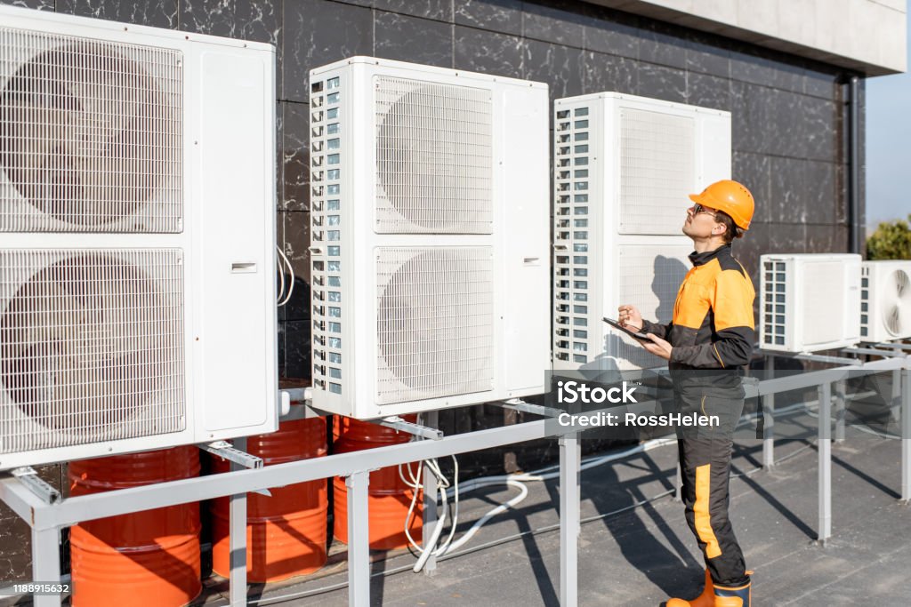 Workman servicing air conditioning or heat pump with digital tablet Professional workman in protective clothing adjusting the outdoor unit of the air conditioner or heat pump with digital tablet Air Conditioner Stock Photo