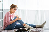 attractive woman with pain in knee sitting on bed in apartment