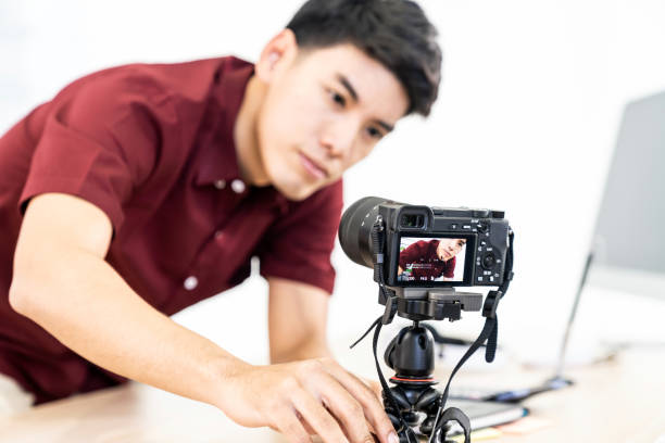 Vlogger blogger set up live camera Young asian male blogger setting up camera for recording live vlog video tutorial session at home. IT blogging or vlogging, social media hobby broadcasting, or online learning course concept. Focus on camera home recording studio setup stock pictures, royalty-free photos & images