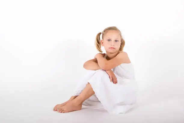7 year old blond Girl, wearing a white dress, sitting and looking at the camera