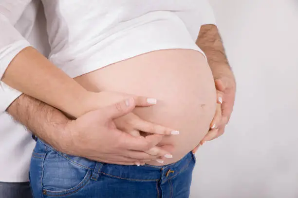 Couple holding pregnant belly on white background