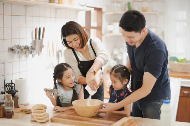 Photo of Young Asian love family are preparing the dough powder, cookies, cake on table in the kitchen which Excited smiling and felling happy. parent and daughter are cooking on the day at home.