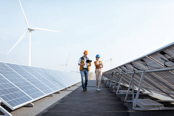 Engineers on a solar power plant View on the rooftop solar power plant with two engineers walking and examining photovoltaic panels. Concept of alternative energy and its service power equipment stock pictures, royalty-free photos & images