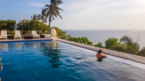 Lombok - A woman enjoying the sunset in an infinity pool A young woman leaning at the edge of an infinity pool and looking at the sun setting into the sea. There is a big palm tree in front. Calmness and serenity. Luxury hotel in Lombok, Indonesia. gili trawangan stock pictures, royalty-free photos & images