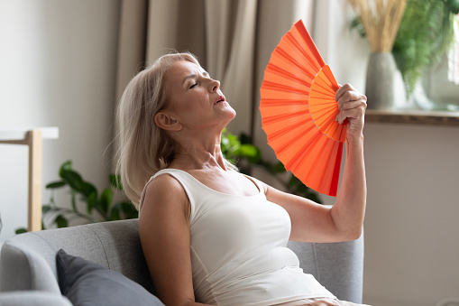 Anciana estresada que agita ventilador sufre de sobrecalentamiento en casa photo