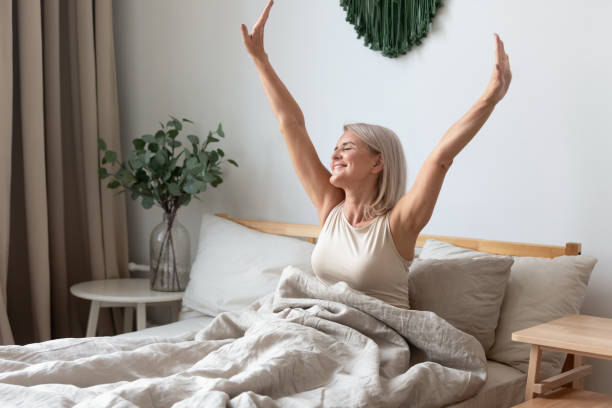 Happy mature woman stretching in bed waking up happy concept Happy fresh mature middle aged woman stretching in bed waking up alone happy concept, smiling old senior lady awake after healthy sleep sitting in cozy comfortable bedroom interior enjoy good morning person waking up stock pictures, royalty-free photos & images