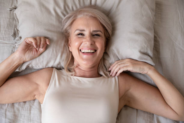 Happy older woman wake up in bed, top view
