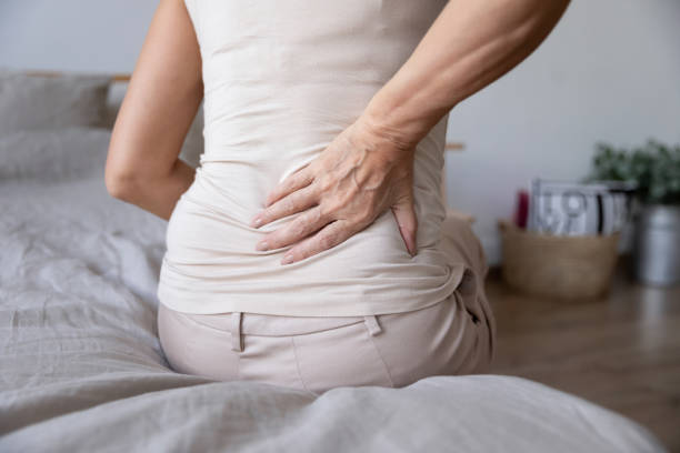 vieja mujer madura sentarse en la cama toque espalda sensación de dolor de espalda - backache chiropractic adjustment pain women fotografías e imágenes de stock