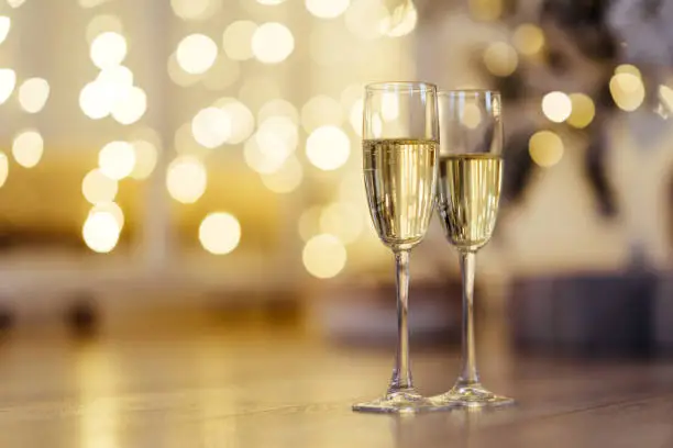 Photo of Two glasses of champagne with lights in the background.