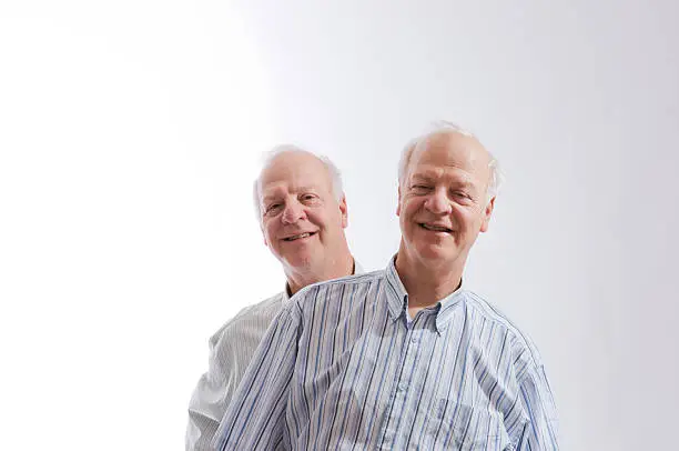 Two older identical twin smiling males leaning opposite directions.