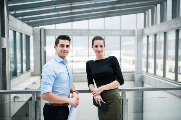 istock Two young architects with blueprints standing in office, looking at camera. 1188944477