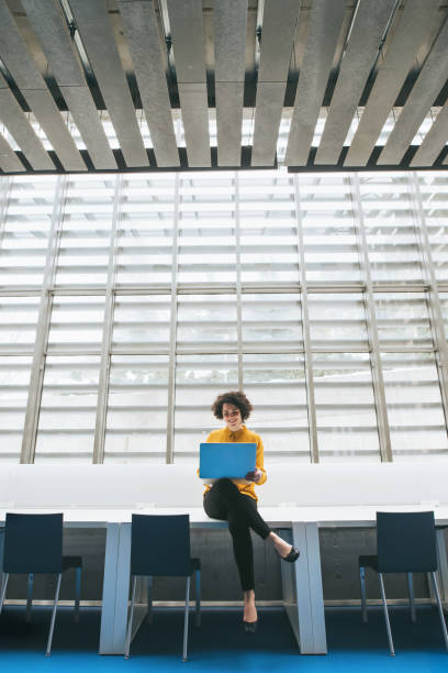 jeune étudiant ou femme d'affaires s'asseyant sur le bureau dans la salle dans une biblioth�èque ou un bureau, utilisant l'ordinateur portatif. - large file photos et images de collection