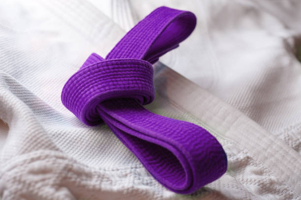 cintura jiu jitsu brasiliana legata in un nodo che giace sull'uniforme bjj bianca - purple belt foto e immagini stock