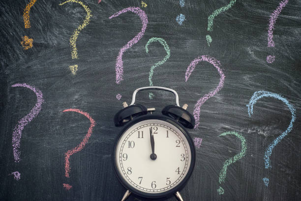 istock Alarm clock standing against blackboard with colorful question marks 1188949872