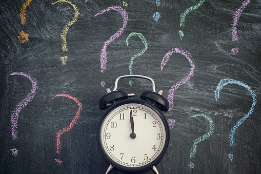 Alarm clock standing against blackboard with colorful question marks. Few minutes before deadline. Close up.