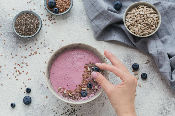 Woman's Hands holding pink yogurt smoothie bowl made with fresh berry and seeds Woman's Hands holding blueberry for decorating pink yogurt smoothie bowl made with fresh blueberry and seeds. Top view eating chia seeds stock pictures, royalty-free photos & images
