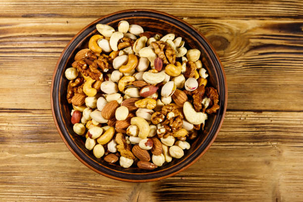 istock Mixed nuts on wooden table. Walnuts, pistachio, almond, peanut, cashew, hazelnut in ceramic bowl. Healthy eating concept. Top view 1188958733