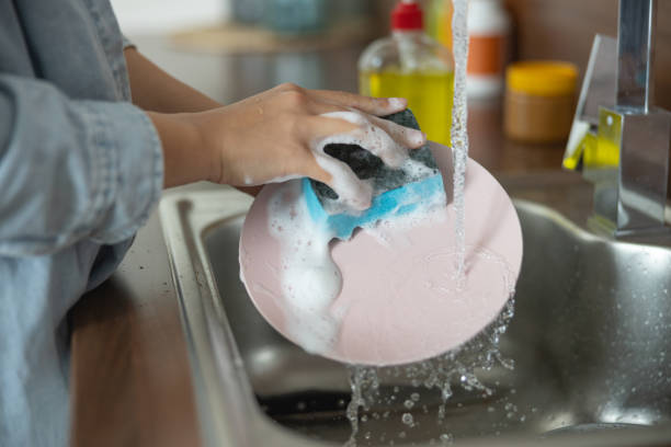Housewife holding a sponge in the hand Close up of female hands cleaning a dirty plate crockery stock pictures, royalty-free photos & images