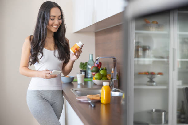 Woman with a dietary supplement in the kitchen Smiling lady looking at the bottle of vitamins in her hand nutritional supplement photos stock pictures, royalty-free photos & images
