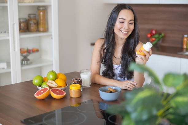 mujer joven tomando un suplemento nutricional en el desayuno - complemento vitamínico fotografías e imágenes de stock