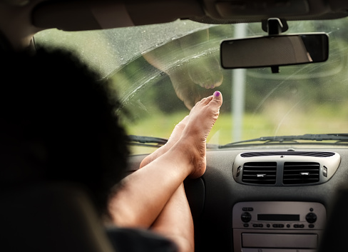 Rear view shot of a woman sitting on passenger seat of a car with her feet up on the dashboard