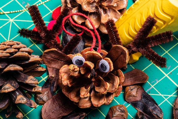 A Macro image of various pine cone reindeer being created.  The pine cones are on a green cutting mat and have googly eyes.