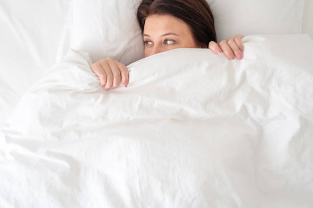 istock woman in bed looking surprised from under blanket 1188971282