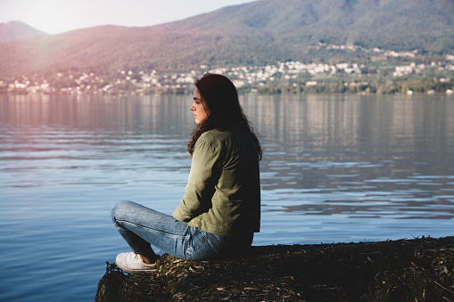 Young pensive woman sitting on the lakeside