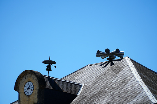 alarm siren on roof of town hall with clock, seen against blue sky