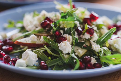 Arugula salad with fresh pomegranate, apple and  soft cow cheese, goat cheese and blue cheese on plate, close up, selective focus
