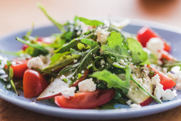 Arugula salad with cherry tomatoes, apple and  soft cow cheese, goat cheese and blue cheese on plate, close up, selective focus