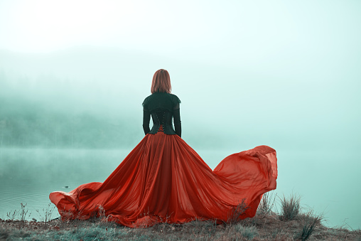 Rear view of woman wearing red skirt posing in fairytale concept at the lake, autumn concept, fog surrounding her