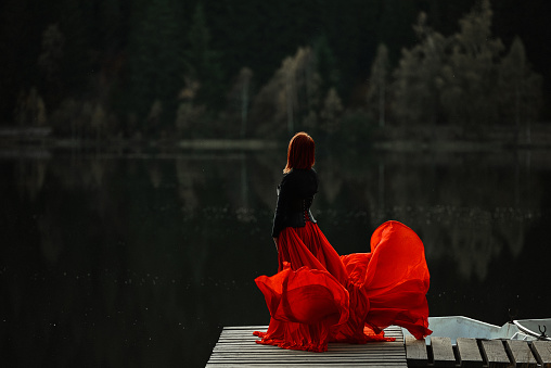 Woman wearing flying red skirt posing in fairytale concept at the lake, autumn concept