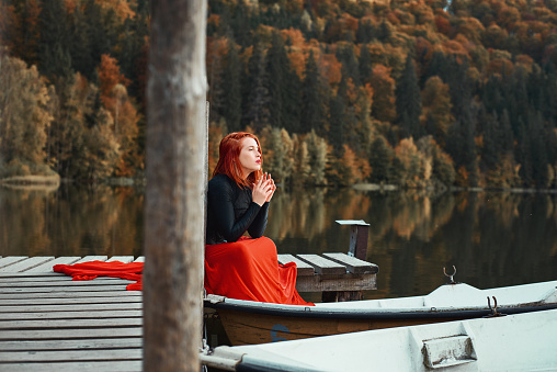 Profile view of woman wearing red skirt posing in fairytale concept at the lake, autumn concept, sitting and thinking
