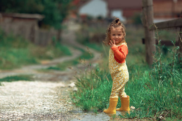 Little baby girl wearing yellow rubber boots playing outside in the mud on a rainy day, splashing