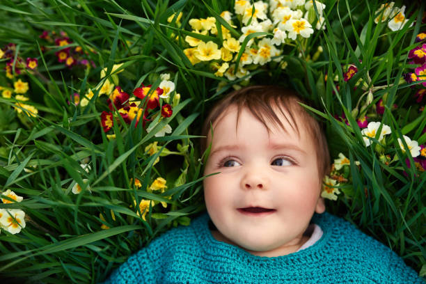 Little baby girl laying on her back in the garden, flowerbed, looking up and smiling