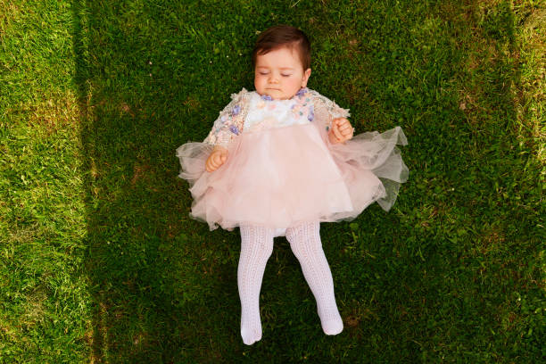 Little baby girl laying down on the grass in the garden, high angle view