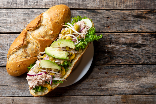 Tuna sub sandwich in rustic baguette with avocado, green olives and sprouts