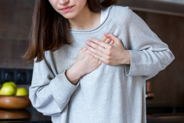 Sick female with heart attack. Health care concept Young woman in grey clothes is holding hands on breast. Brunette girl is feeling bad. Sudden heart attack, myocardial infarction at home. Effect of stress and unhealthy lifestyle concept. coronary artery photos stock pictures, royalty-free photos & images