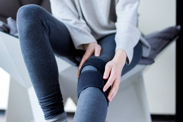 Sick female with compression bandage. Health care concept Closeup female leg in grey leggings dressed in knee brace to help promote recovery of bones, muscles, ligaments. Woman is feeling pain in joints after injury. Arthritis and meniscus diseases concept. tendon photos stock pictures, royalty-free photos & images