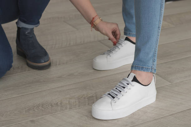 Feet in jeans and white sneakers stand on the wooden floor in the studio. Assistant corrects the items of clothing worn by the model before shooting.