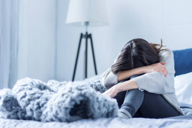 Sick female with depression. Health care concept Young woman in gray clothes is sitting curled up on bed at home. Upset brunette girl is suffering, crying. Depression because of loneliness, stress, problems. Psychological disorders concept. suicide photos stock pictures, royalty-free photos & images