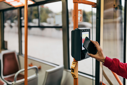 Woman buying tickets in the bus while traveling. Beautiful woman is paying transport ticket with mobile phone.