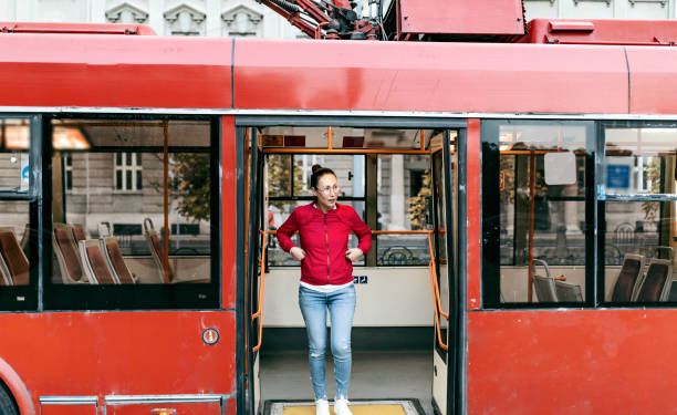 Young positive Asian hipster woman passenger getting off the yellow bus in vacation. Lifestyle and everyday routine concept.