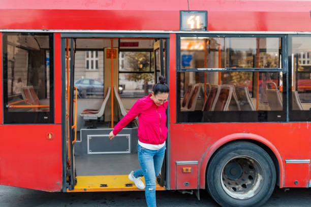 Young positive Asian hipster woman passenger getting off the yellow bus in vacation. Lifestyle and everyday routine concept.
