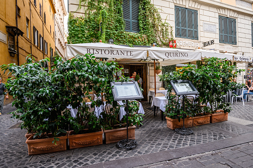 Atmospheric street cafe on a street in the center of Rome. Pots with trees. 28.10.2019 Rome, Italy.