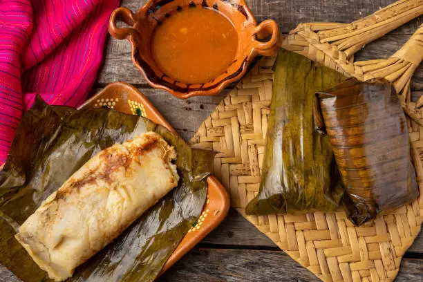 Traditional mexican tamales wrapped in banana leaves also called "oaxaqueños" on wooden background