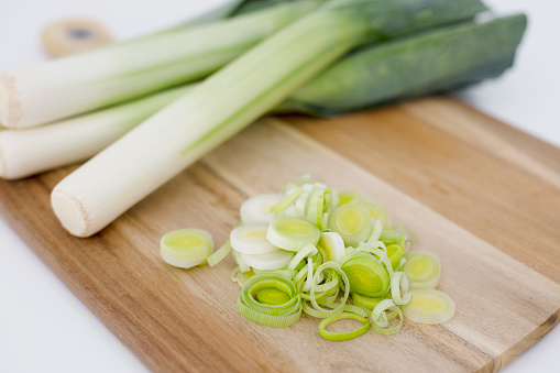 Fresh organic green leeks in a wooden chopping board with leeks cut pieces. Vegan and GMP free