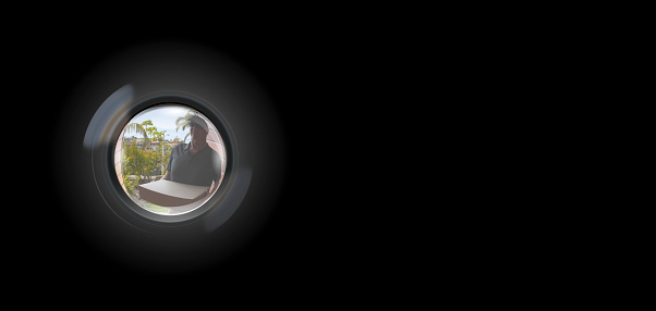 Peephole View of parcel delivery man outside door to entry security surveillance concept solid black background