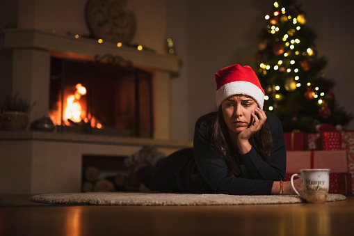 Young woman laying on carpet alone at home around fireplace and Christmas decoration on background.